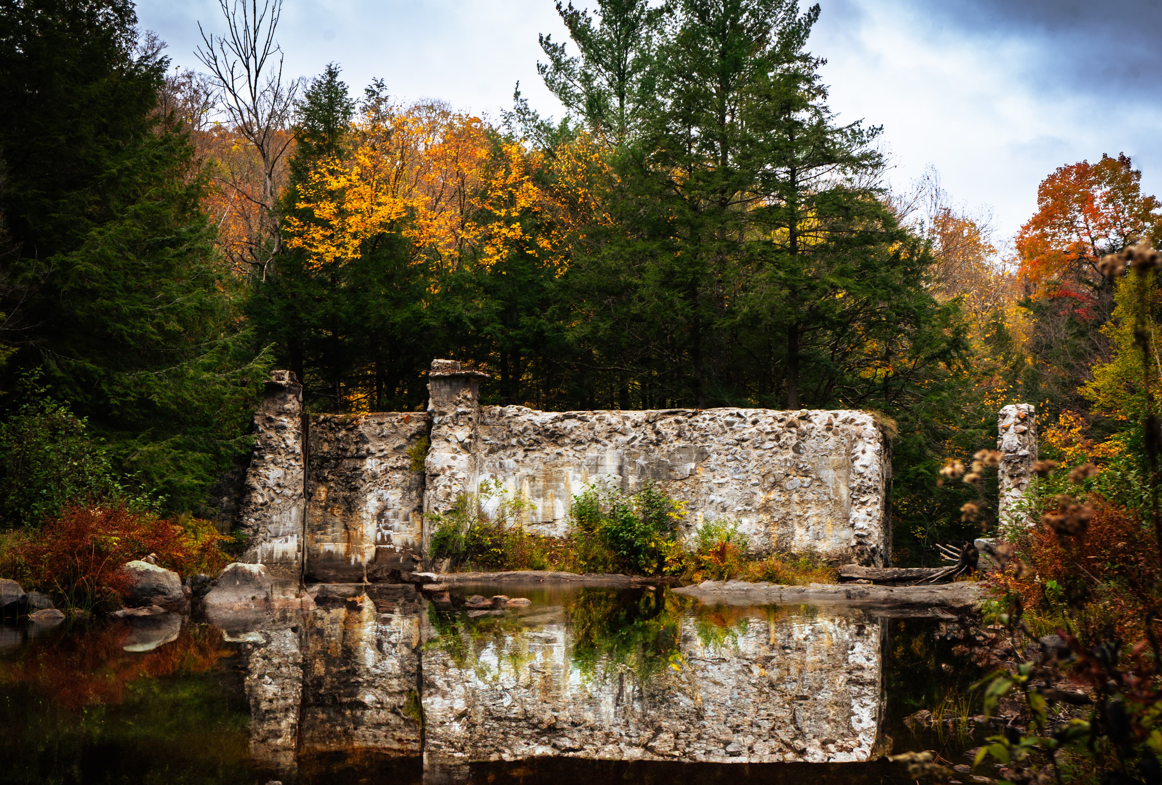 An old stone ruin reflected in still water, surrounded by autumn trees