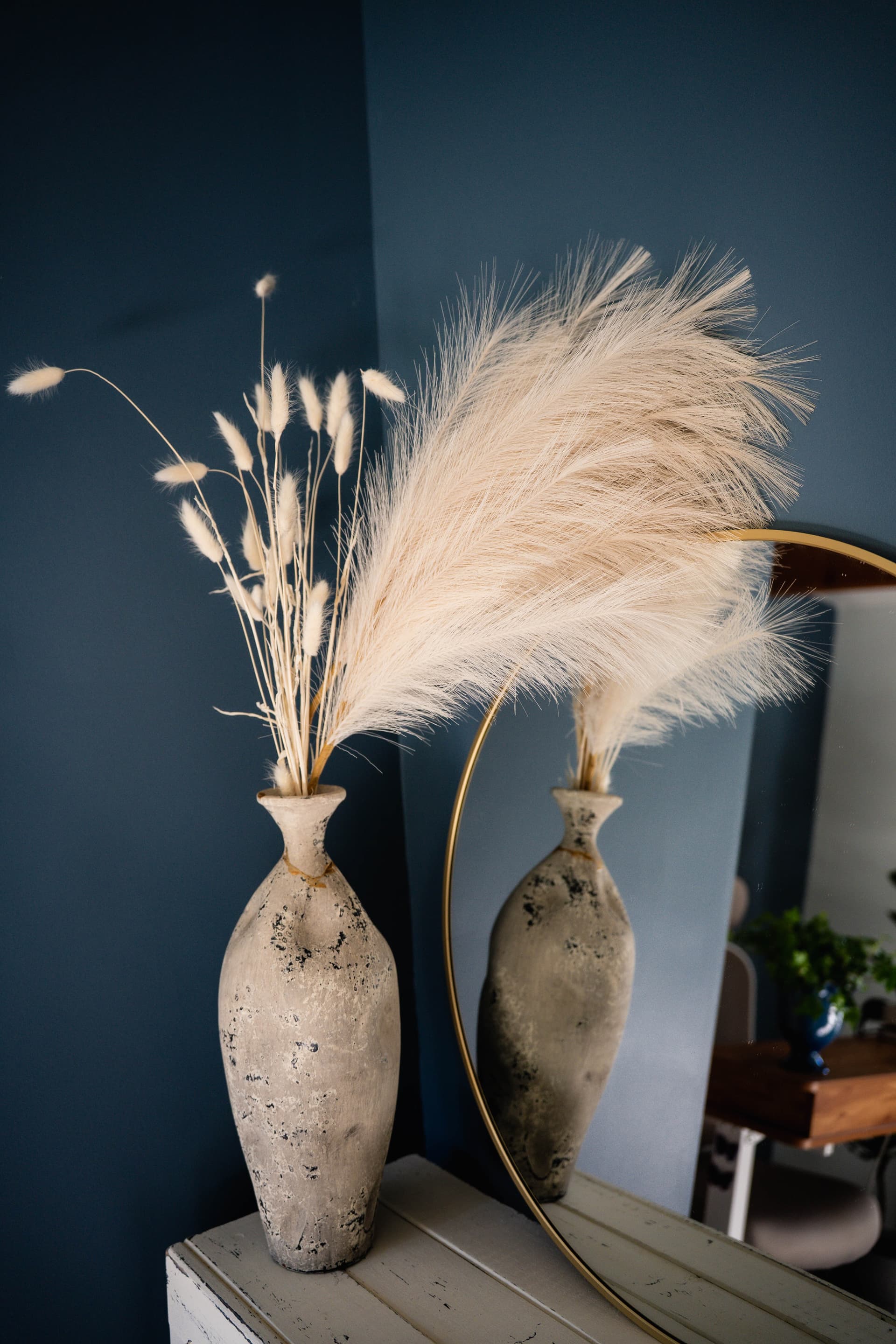 Pampas grass in a vase against a blue wall, reflected in a gold mirror