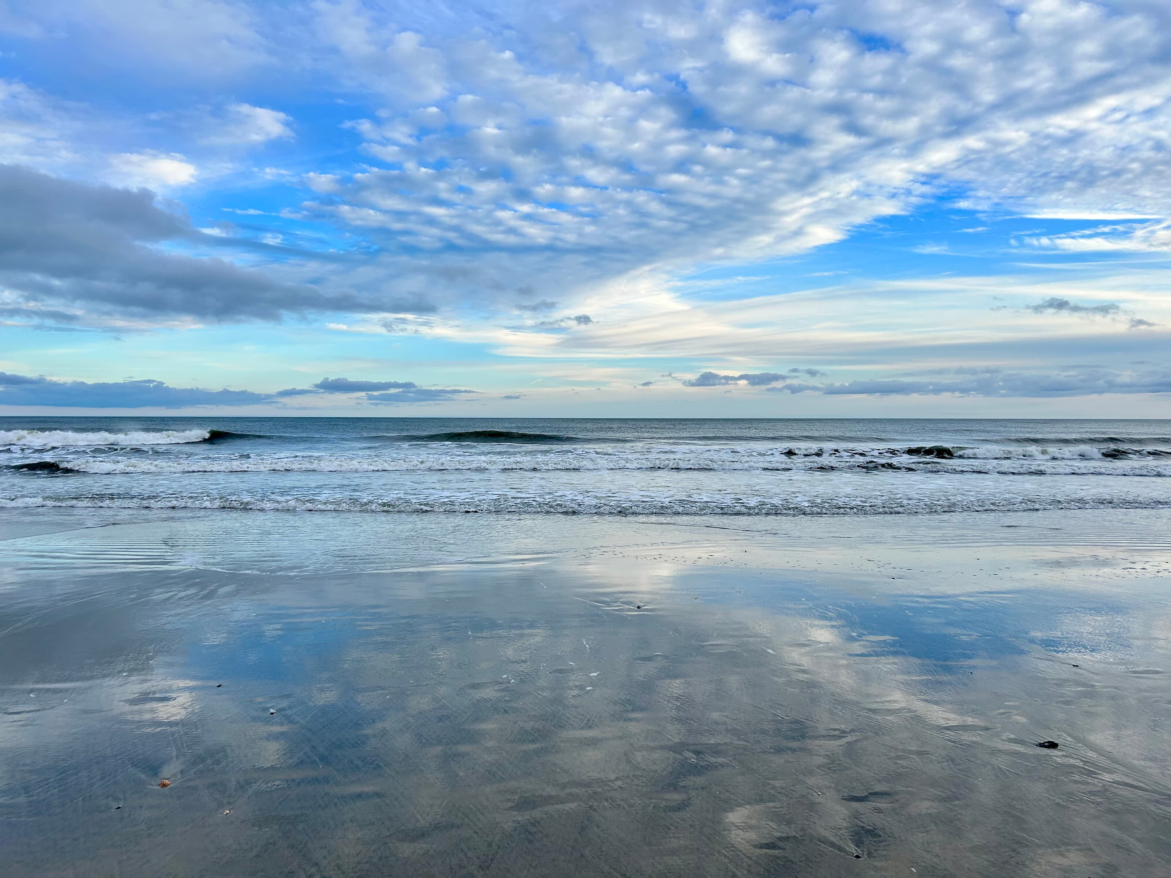 A wide ocean horizon reflected on wet sand